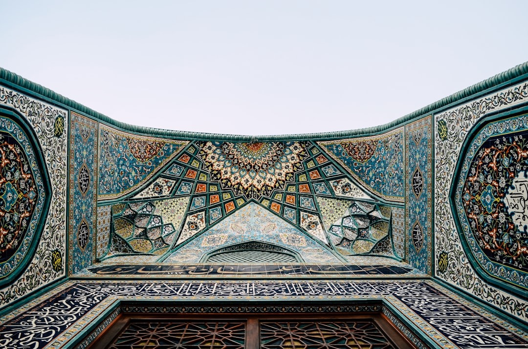 Intricate teal and gold Islamic geometric tilework archway against a blue sky.