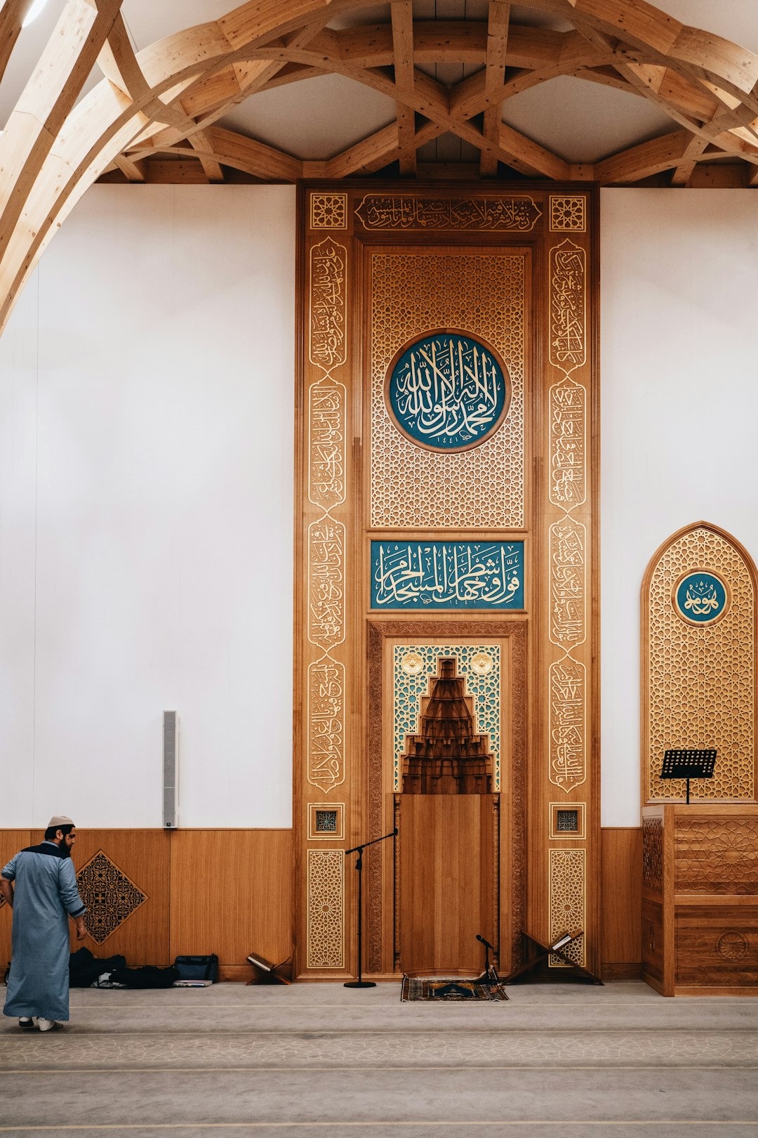 Man walks towards intricately carved wooden mihrab in mosque.
