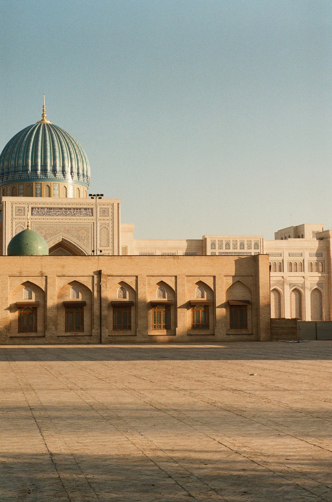 Islamic architectural complex with blue and green domes under a bright sky.
